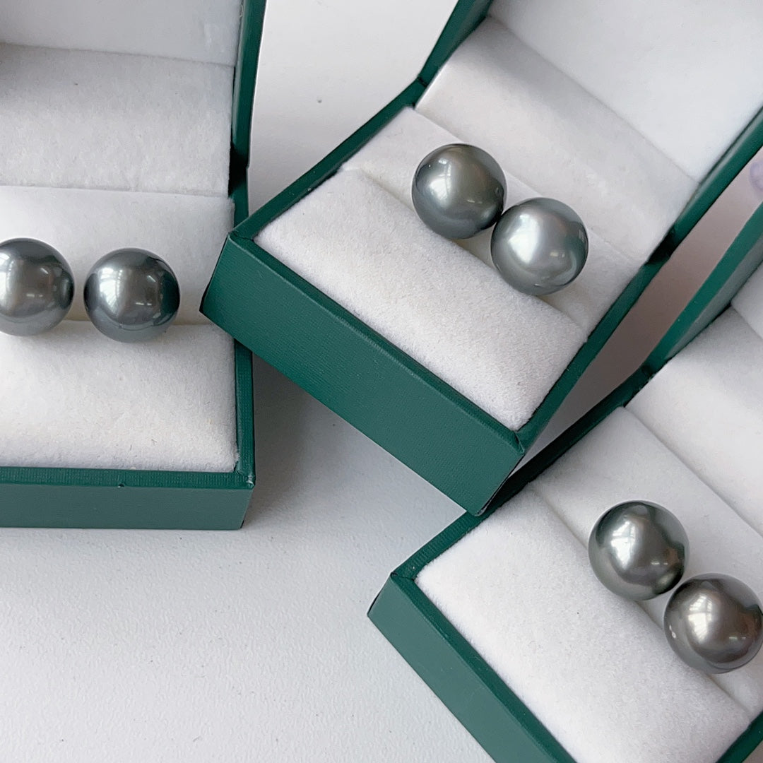 Kiiltävät 12-13 mm Tahitian Pearl -korvakorut 18K kultaa suurella levyn taustalla